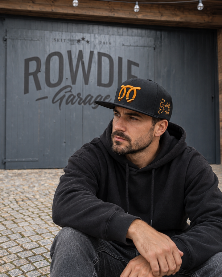 Mann trägt schwarze AsphaltRowdies Selbstzünder Snapback vor der Rowdie Garage